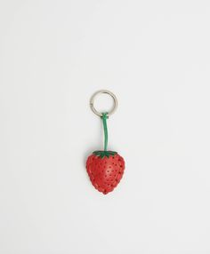 a strawberry shaped keychain hanging from a green string on a white surface,