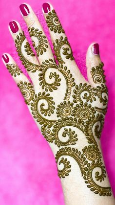 a woman's hand with henna on it and pink wall in the background