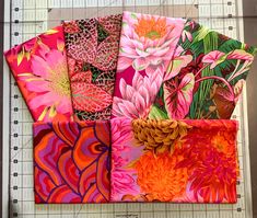 four square pieces of fabric with flowers and leaves on them, laid out on a cutting board