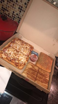 an open pizza box on top of a stove with cheese and bread in the bottom