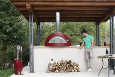 a man standing next to a pile of firewood in front of a pizza oven