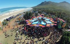 an aerial view of people gathered at the beach with tents and umbrellas set up