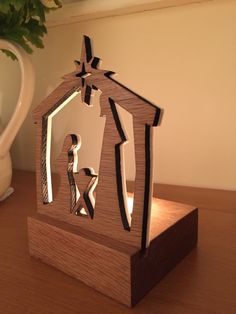 a nativity scene made out of wood on a table next to a potted plant