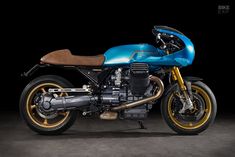 a blue and gold motorcycle parked on top of a cement floor next to a black background