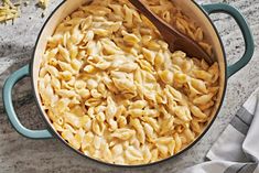 a pot filled with macaroni and cheese on top of a counter next to a wooden spoon