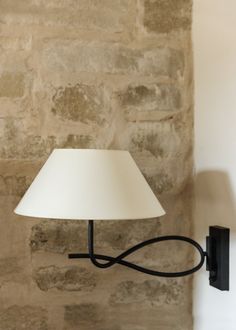 a lamp on a wall next to a stone wall with a white shade hanging from it