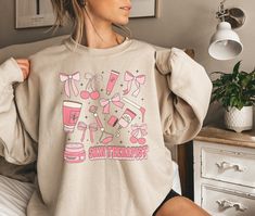 a woman sitting on top of a bed wearing a sweatshirt with pink items printed on it