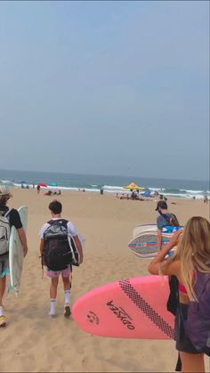 people walking on the beach with surfboards and backpacks in their hands, one person carrying a surfboard