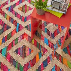 a red table topped with a potted plant next to a colorful rug