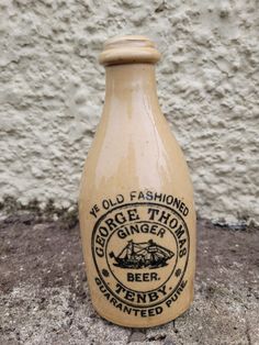 an old fashioned ginger beer bottle is sitting on the ground next to a white wall