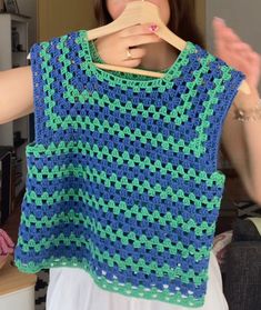 a woman holding up a blue and green crocheted top