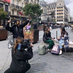 people are sitting on benches in the middle of a city square, taking pictures with their cameras