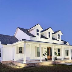 a white two story house with black roof and shutters on the front door is lit up at night