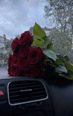 a bouquet of roses sitting on the dashboard of a car in front of a rain soaked window