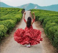 a woman in a red dress is walking down a dirt road with her arms up