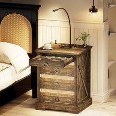 a nightstand with a lamp on top of it next to a bed