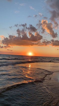 the sun is setting over the ocean with clouds in the sky and waves on the beach