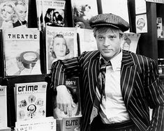 a man in a suit and hat leaning against a wall with posters on the walls behind him