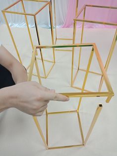 a person is pointing at some gold geometric structures on the floor with one hand and two fingers in front of them