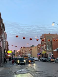 cars are parked on the street in front of buildings with lanterns hanging above them at dusk