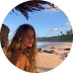 a beautiful young woman standing on top of a sandy beach next to the ocean under a thatched umbrella