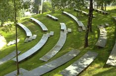 a bunch of benches sitting on top of a lush green hillside next to trees and grass