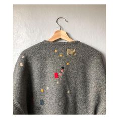 a gray sweater with small squares and letters on the back, hanging from a hanger