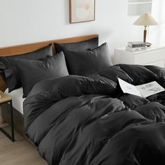 a bed with black comforter and pillows in a room next to a lamp on a table