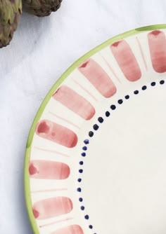 a plate with pink and green designs on it next to two pineapples in the background