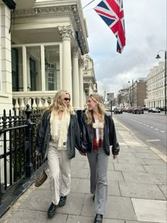 two women are walking down the sidewalk with an union jack flag flying in the background