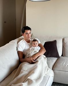 a man holding a baby wrapped in a blanket sitting on a white couch next to a lamp