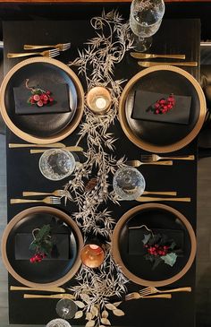 a black and gold table setting with plates, silverware and holly berries on it