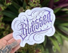 a hand holding up a sticker with the word bluebird written in purple ink