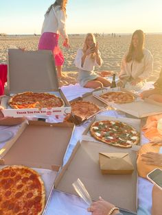 several people sitting on the beach eating pizza