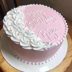 a pink birthday cake with white frosting and flowers on top is sitting on a wooden table