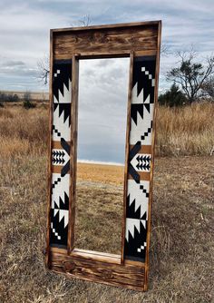 a wooden mirror sitting on top of a dry grass field next to an empty field