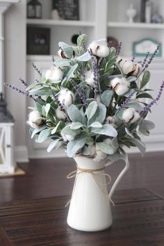 a white vase filled with flowers and greenery on top of a wooden table next to a book shelf