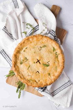 a freshly baked pie on a wooden cutting board with rosemary sprigs in the crust