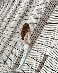 a woman leaning against a wall in front of a building with lots of white tiles on it