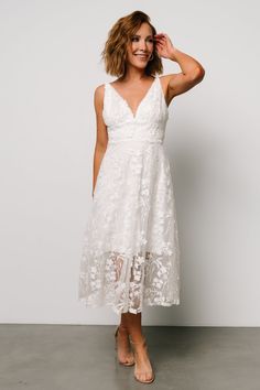 a woman in a white dress posing for the camera with her hand on her head