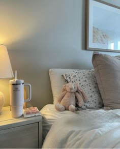 a teddy bear sitting on top of a bed next to a night stand and lamp