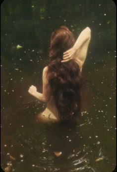 a woman is sitting in the water with her back turned to the camera and she has long dark brown hair