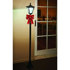 a lamp post with a red bow on it next to an open door and window