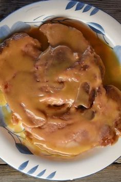 a white plate topped with meat covered in gravy on top of a wooden table