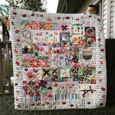 a woman standing next to a quilted wall hanging on the side of a house