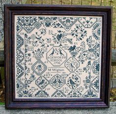 a cross stitch sample in a frame on a bench