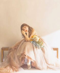 a woman sitting on top of a wooden bench wearing a dress and holding a bouquet