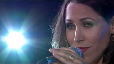 a woman holding a microphone in her right hand and looking at the camera with bright lights behind her