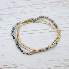 three beaded bracelets with gold and black beads on a white wooden table top