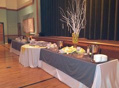 two tables with food on them in front of a black drapeed wall and wooden floors